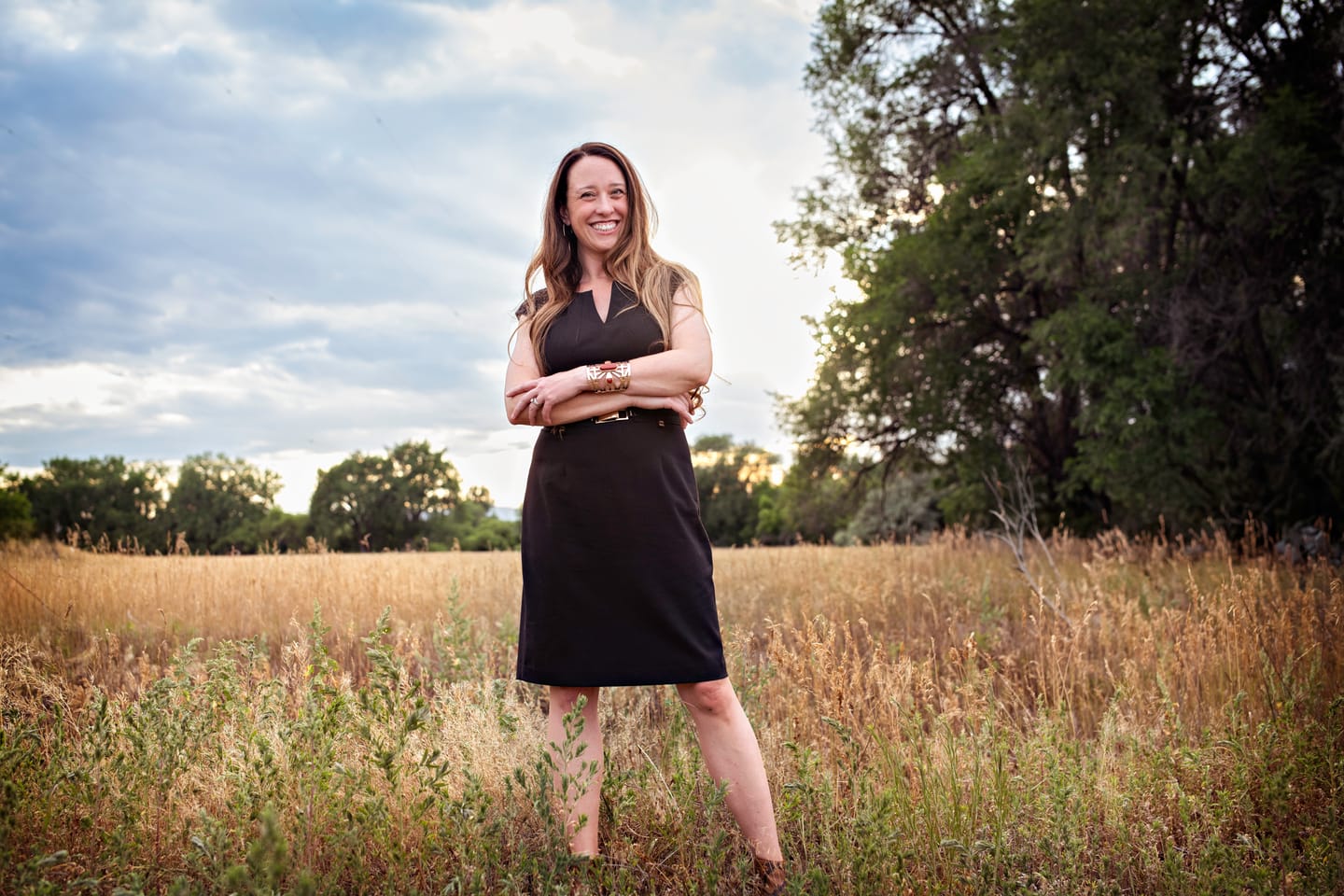 Stephanie Drobny standing in an open prairie field, arms crossed, under a wide sky